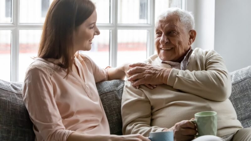 Smiling young woman sitting on sofa with happy older man having a cup of tea