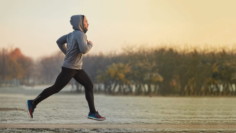 Young athletic man running at park during cold autumn morning