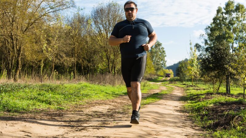 A man jogging through a park, on a sunny day.