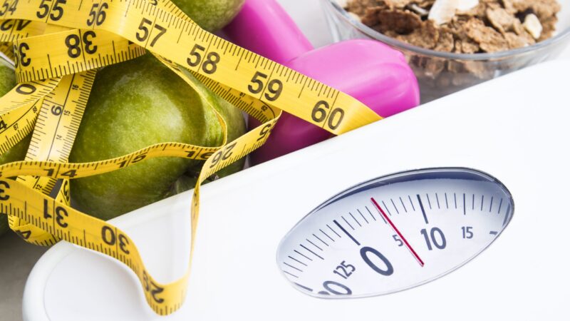 scale with cereals, fruit, weight and tape measure and concept of diet and healthy lifestyle