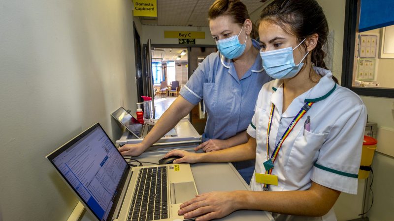 Two female nurses wearing face masks looking at a laptop screen